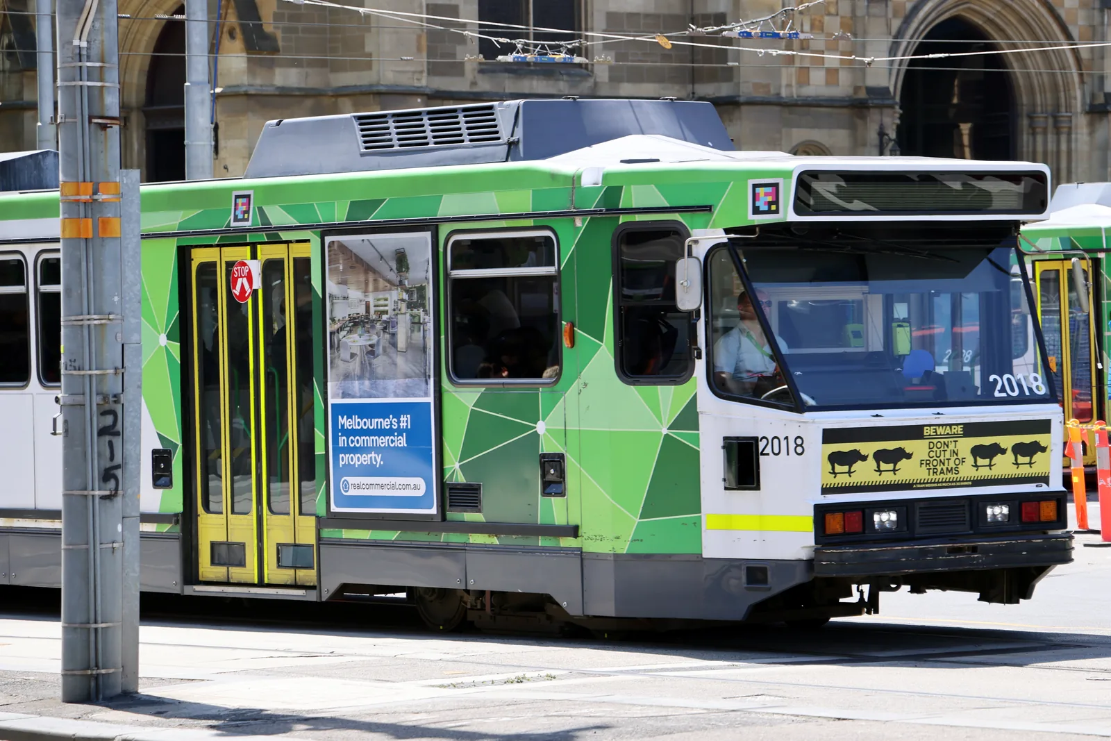 A green and yellow Melbourne tram on a city street