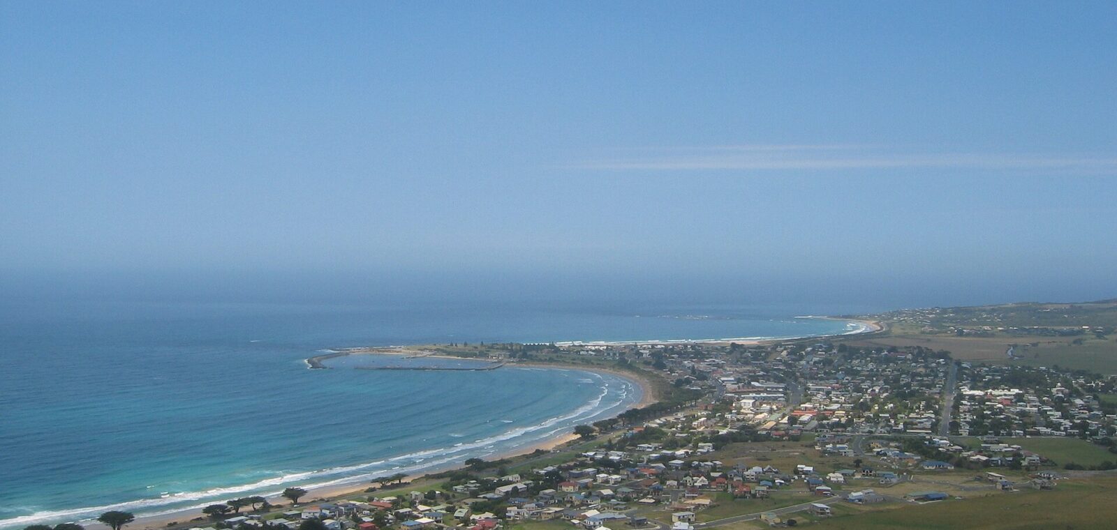 Apollo Bay seen from Mariners Lookout, with the curved beach, harbour breakwater and town spread below green hills