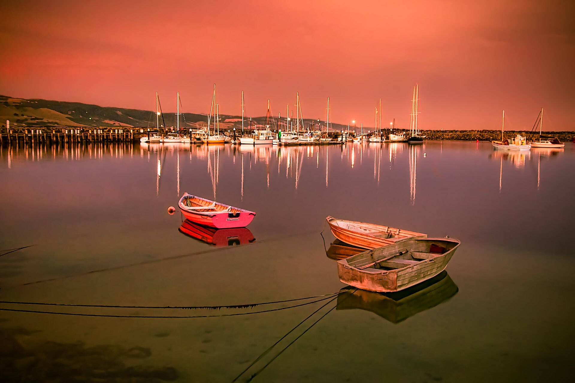 Small dinghies and yachts moored on still water in Apollo Bay harbour under a pink evening sky