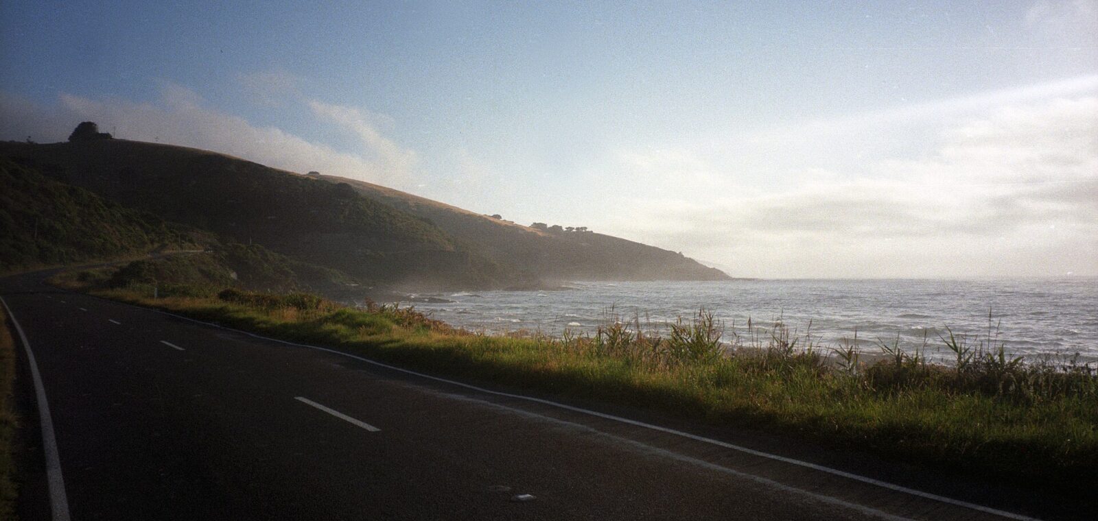 The Great Ocean Road curving along a grassy shoreline beside the Southern Ocean under a pale sky