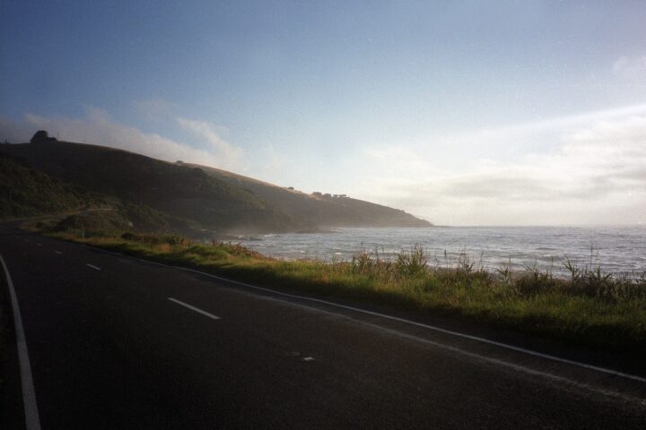 The Great Ocean Road curving along a grassy shoreline beside the Southern Ocean under a pale sky