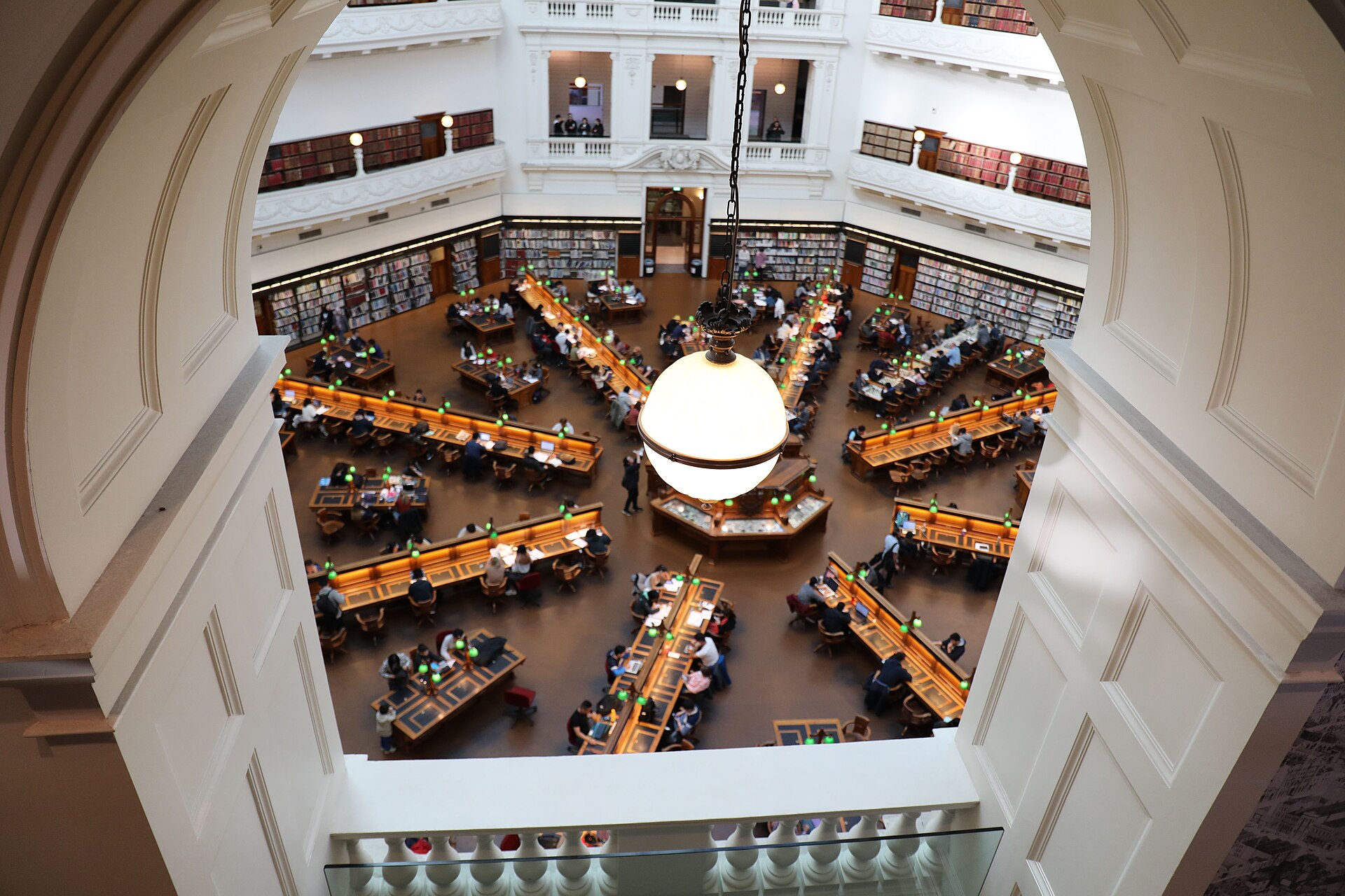 View through an arched opening down into the octagonal La Trobe Reading Room, with desks radiating from the centre and green reading lamps