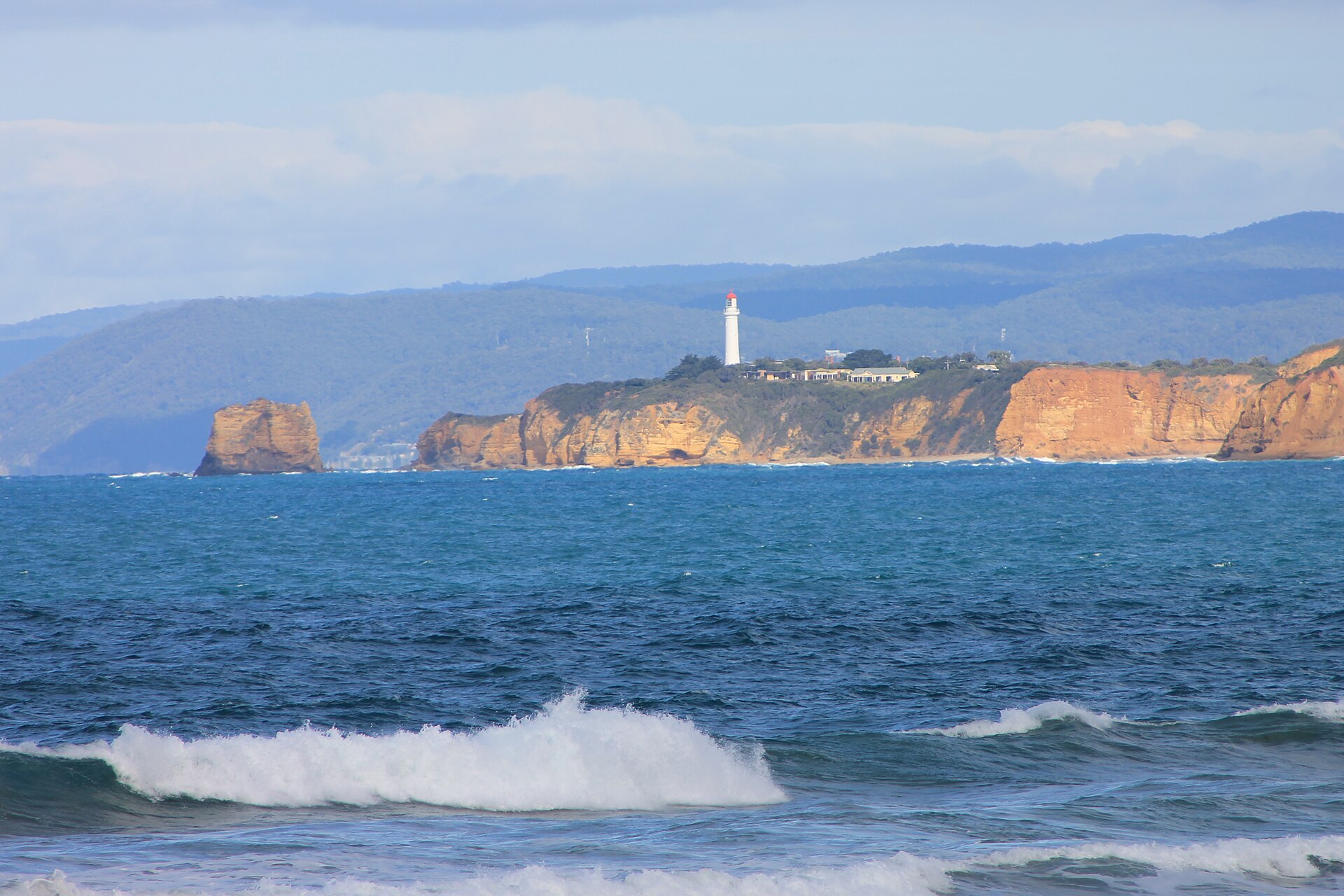 Split Point Lighthouse, white with a red cap, on orange sandstone cliffs at Aireys Inlet with the Otway Ranges behind