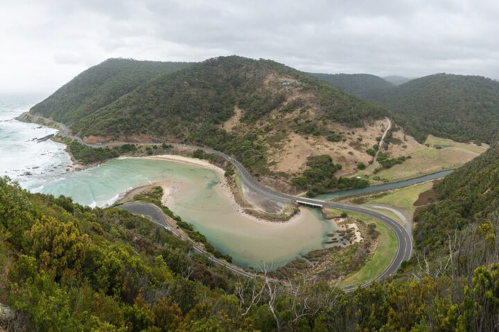 The Great Ocean Road curving around the mouth of the St George River below forested hills, seen from Teddy's Lookout at Lorne