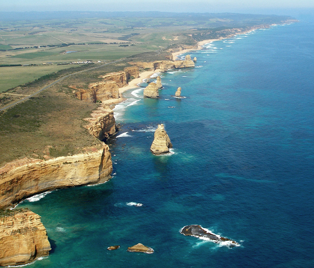 Aerial view of the Twelve Apostles sea stacks and golden limestone cliffs stretching along the coast, seen from a helicopter