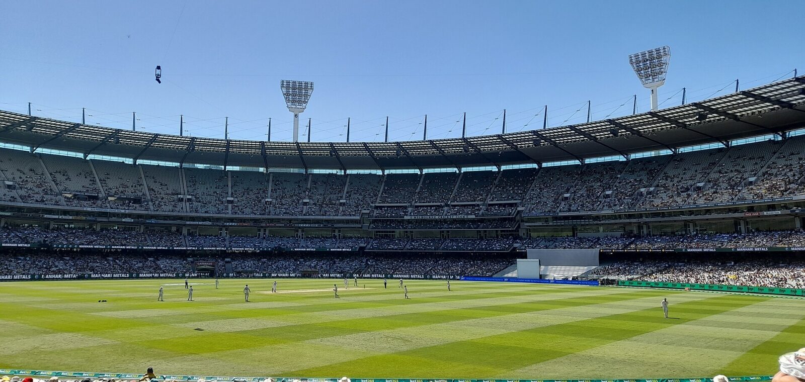 Spectators in hats in the MCG's Members' Reserve look out over a Test match on the green oval under a blue December sky