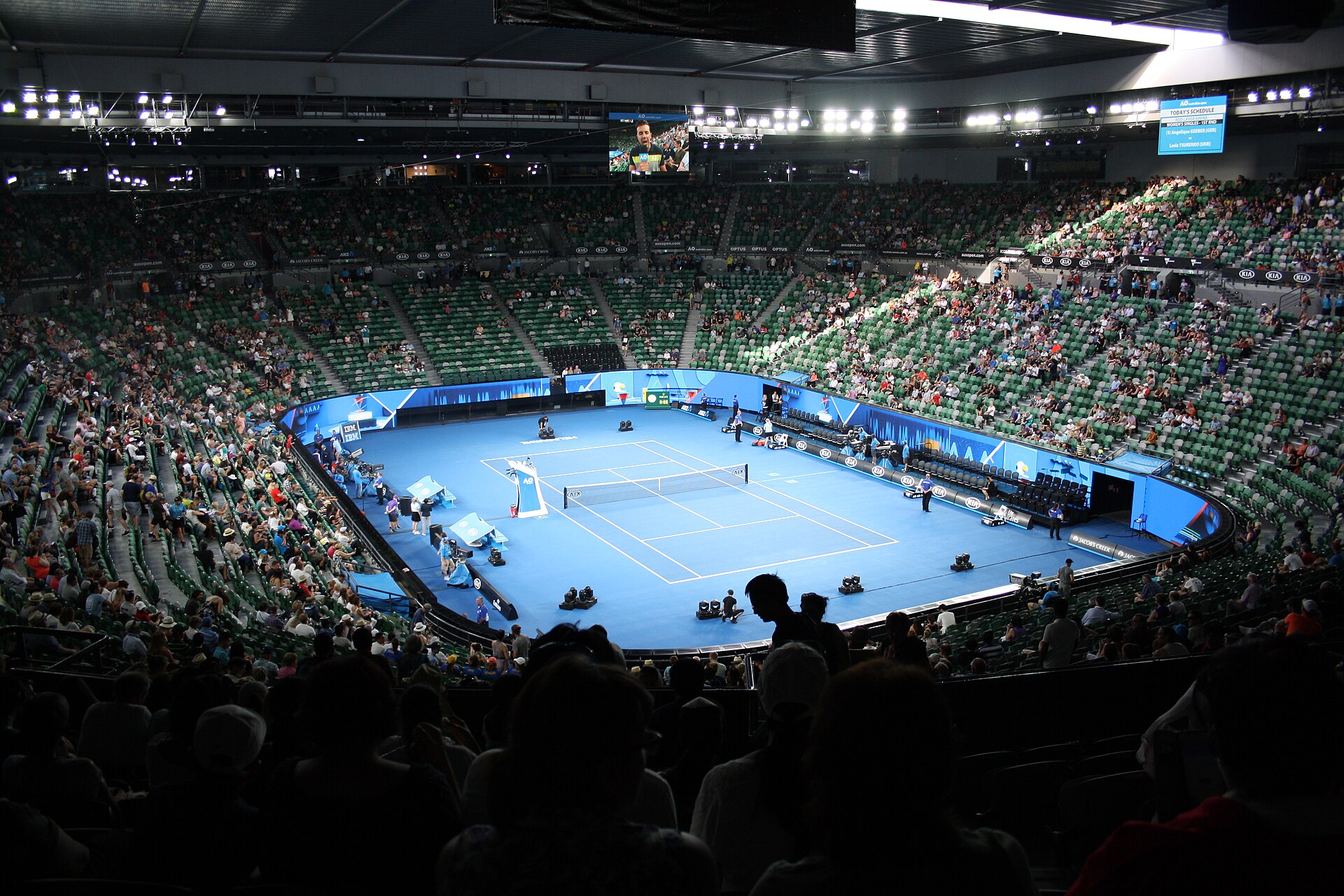 Inside Rod Laver Arena with its roof closed, the blue hard court under lights and the stands full for an Australian Open match
