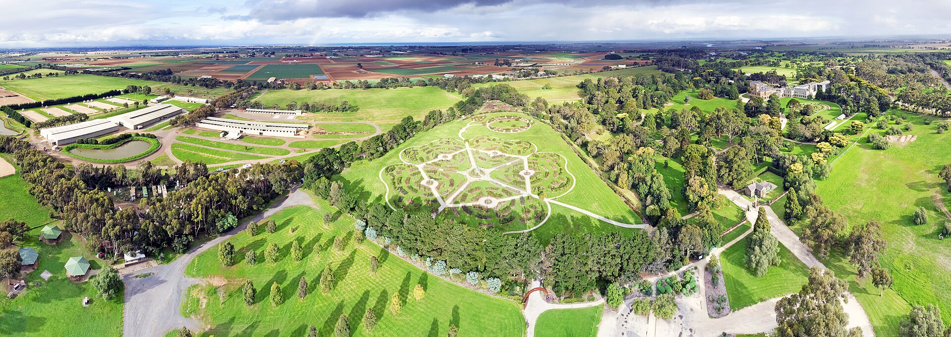 Aerial view of Werribee Park with the patterned beds of the rose garden among lawns and trees, and farmland stretching to the horizon